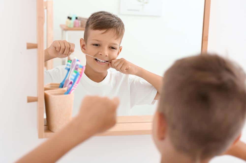 child-flossing-teeth-in-mirror boy flossing teeth while looking mirror