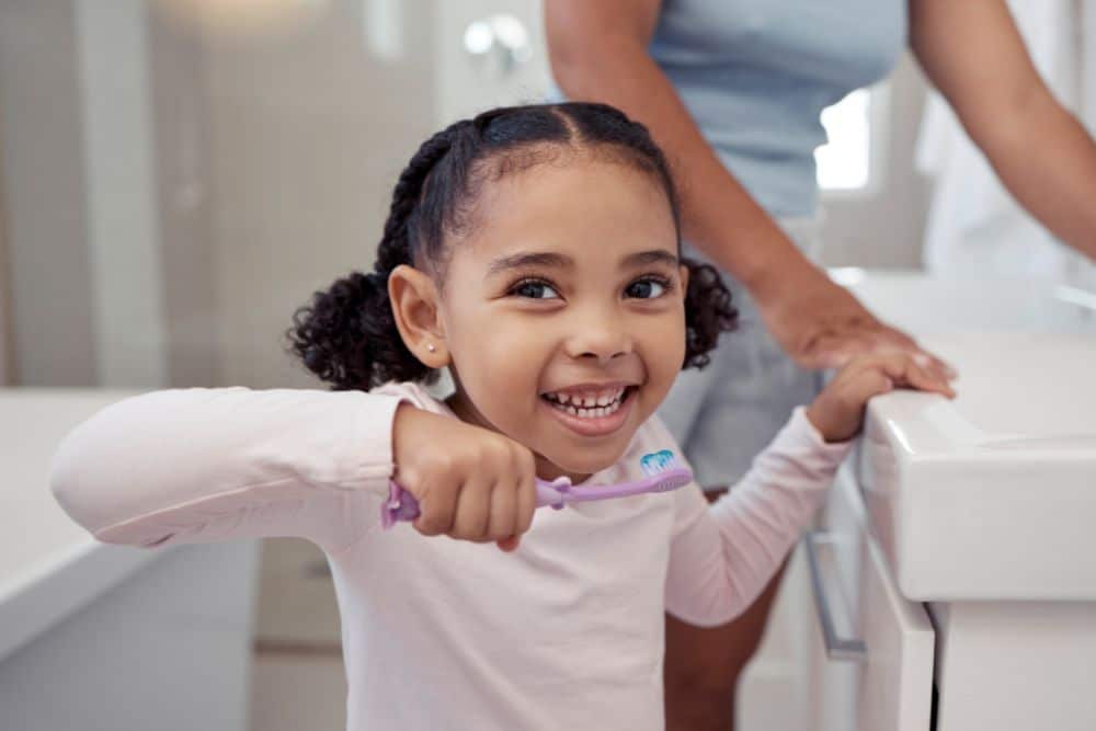 young-girl-brushing-teeth-fluoride-toothpaste girl brushing teeth with parent in bathroom